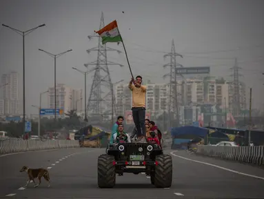 Seorang petani mengibarkan bendera India saat ia berdiri di atas kap kendaraan di jalan bebas hambatan utama di Ghazipur, pinggiran New Delhi, India, Kamis (9/12/2021). Ribuan petani India menghentikan protes mereka selama setahun pada Kamis setelah pemerintah mencabut undang-undang pertanian yang k