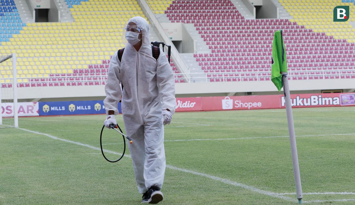 Petugas berkeliling lapangan untuk menyemprot cairan disinfektan sebelum pertandingan antara Persikabo 1973 melawan Arema FC pada laga Piala Menpora di Stadion Manahan, Solo, Minggu (21/3/2021). (Bola.com/M Iqbal Ichsan)