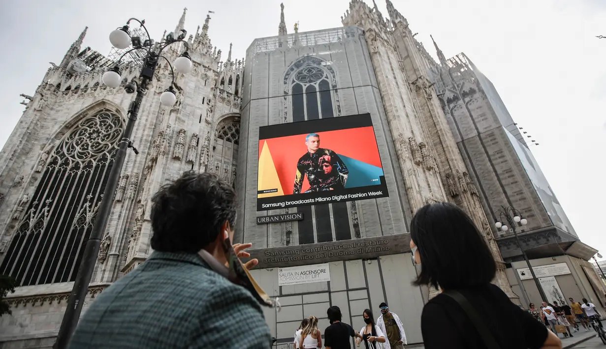 Pejalan kaki melewati layar di katedral Duomo yang menunjukkan model Moschino selama Milan Digital Fashion Week, di Milan, Italia, 14 Juli 2020. Empat puluh rumah mode menampilkan koleksi pakaian untuk musim semi/musim panas 2020 dalam format digital di tengah pandemi Covid-19. (AP Photo/Luca Bruno)