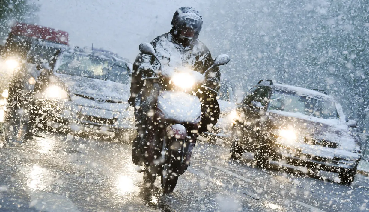 Pengendara motor melintasi hujan salju di Munich, Jerman selatan, (18/4). Hujan salju yang melanda kawasan ini tidak menyurutkan warga untuk tetap beraktivitas. (AFP PHOTO / dpa / Tobias Hase / Jerman OUT)