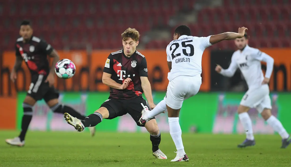 Gelandang Bayern Munchen, Joshua Kimmich, berusaha menghalau tendangan gelandang Augsburg, Carlos Gruezo, dalam laga lanjutan Liga Jerman di WWK Arena, Kamis (21/1/2021) dini hari WIB. Bayern Munchen menang 1-0 atas Augsburg. (AFP/Andreas Gebert/pool)