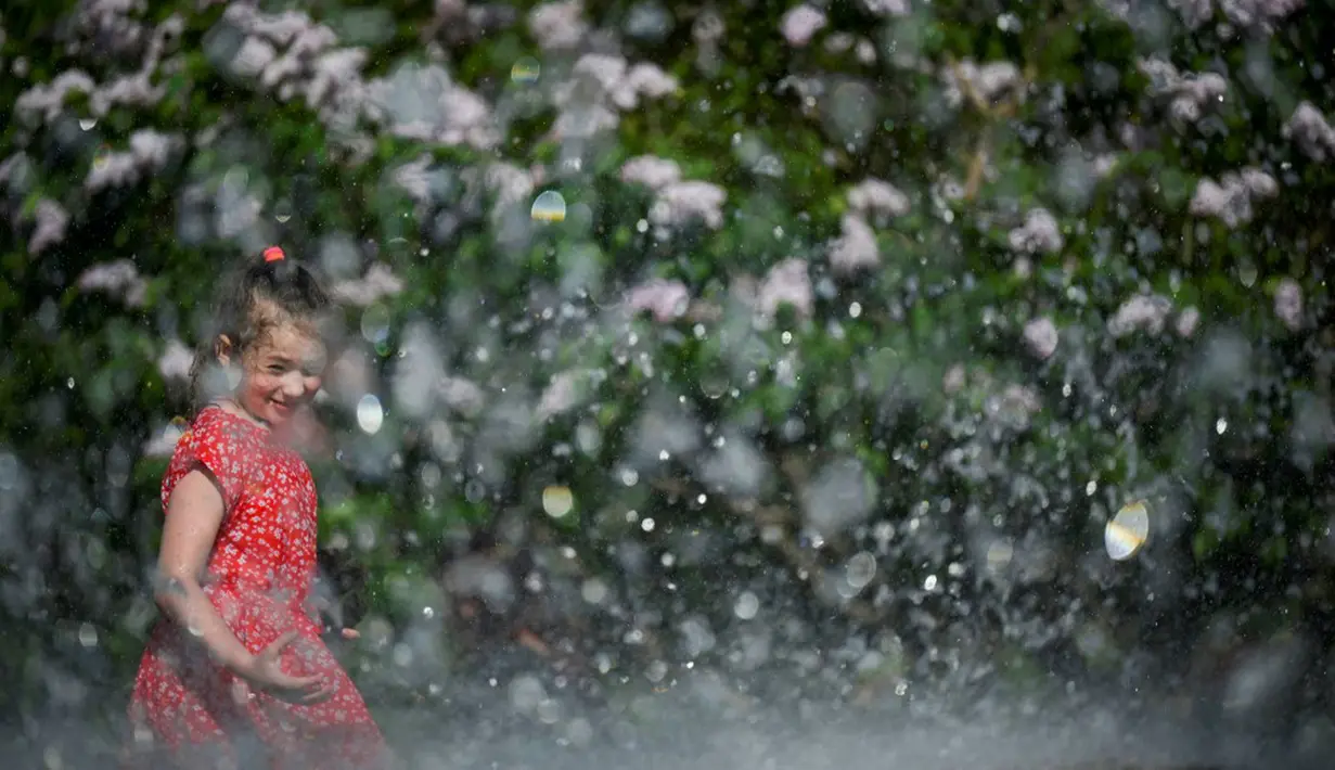 Seorang gadis mendinginkan diri di air mancur saat musim semi yang panas di Moskow, Rusia, Selasa (18/5/2021). Suhu di Moskow telah mencapai 31 derajat Celcius. (Natalia KOLESNIKOVA/AFP)