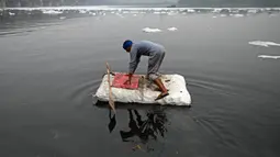 Seorang pria bersiap mendayung rakitnya untuk mengumpulkan bahan daur ulang dekat potongan busa tercemar yang mengambang di Sungai Yamuna, New Delhi, India, 26 Desember 2021. Sungai Yamuna mengalir sekitar 1.378 kilometer ke selatan dari Himalaya, melewati sejumlah negara bagian.(Sajjad HUSSAIN/AFP)