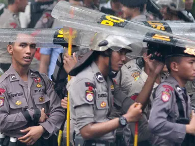 Petugas kepolisian menggunakan tameng untuk berteduh dari hujan saat menjaga aksi Hari Buruh di Jalan Medan Merdeka, Jakarta, Senin (1/5). (Liputan6.com/ Yoppy Renato)