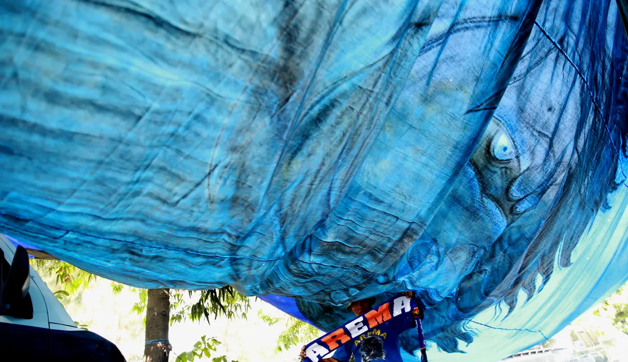 Bendera raksasa disulap jadi tempat berteduh sekelompok Aremania saat menyatroni Solo, Minggu (11/10/2015). Mereka datang untuk mendukung Arema yang menjajal Sriwijaya FC di semifinal kedua Piala Presiden 2015. (Bola.com/Nicklas Hanoatubun)