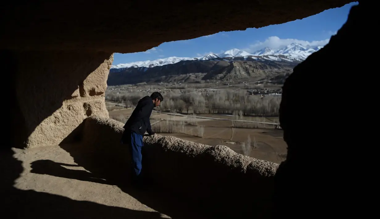 Seorang pria Hazara melihat keluar dari gua lokasi patung Buddha raksasa yang dihancurkan oleh Taliban pada 2001 di Provinsi Bamiyan, Afghanistan, 3 Maret 2021. Patung Buddha Bamiyan diukir pada tebing batu pasir di abad kelima silam. (WAKIL KOHSAR/AFP)