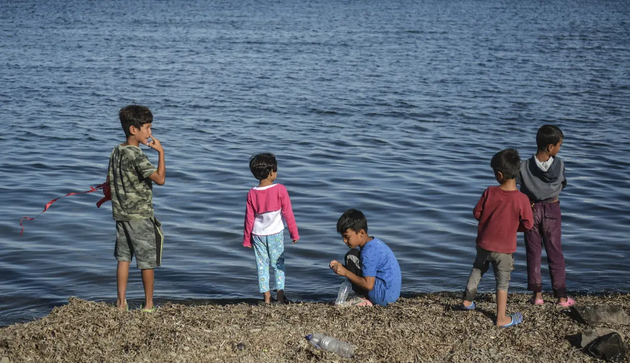 Anak-anak berdiri di tepi laut di kamp pengungsi Kara Tepe, di pulau Lesbos di timur laut Aegean, Yunani (14/10/2020).  Sekitar 7.600 pengungsi dan migran telah menetap di kota tenda baru setelah kebakaran yang menghancurkan kamp pengungsi Moria. (AP Photo/Panagiotis Balaskas)