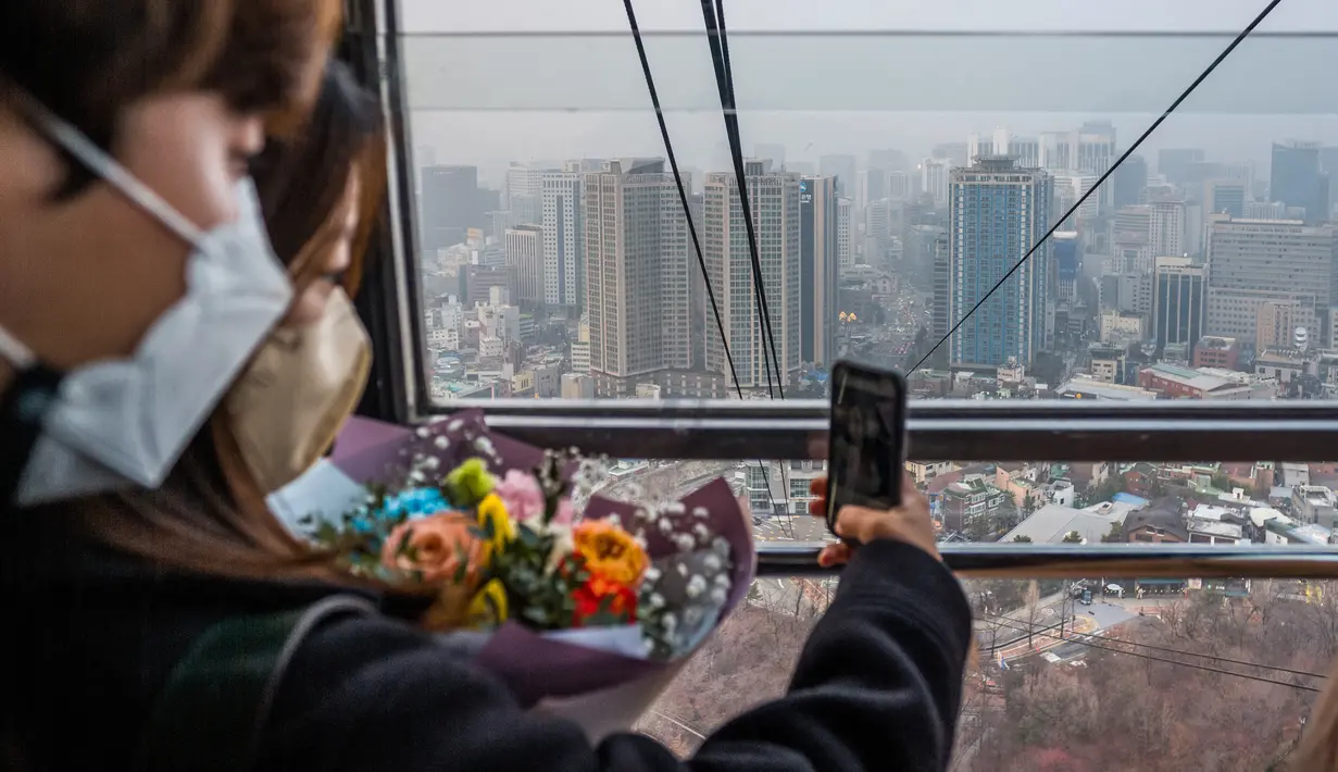 Sepasang kekasih berfoto selfie di dalam kereta gantung saat bangunan di latar belakang terlihat diselimuti kabut, selama kunjungan ke Menara Namsan pada hari yang tercemar di Seoul, Korea Selatan, Rabu (15/12/2021). (AFP/Anthony Wallace)