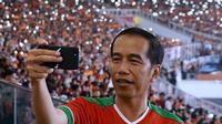 Presiden Joko Widodo (Jokowi) tampak asyik membuat vlog dengan kamera handphone saat menyaksikan laga final Piala Presiden 2018 antara Persija Jakarta vs Bali United di Stadion Utama Gelora Bung Karno, Sabtu (17/2). (Liputan6.com/Pool/Biro Pers Setpres)