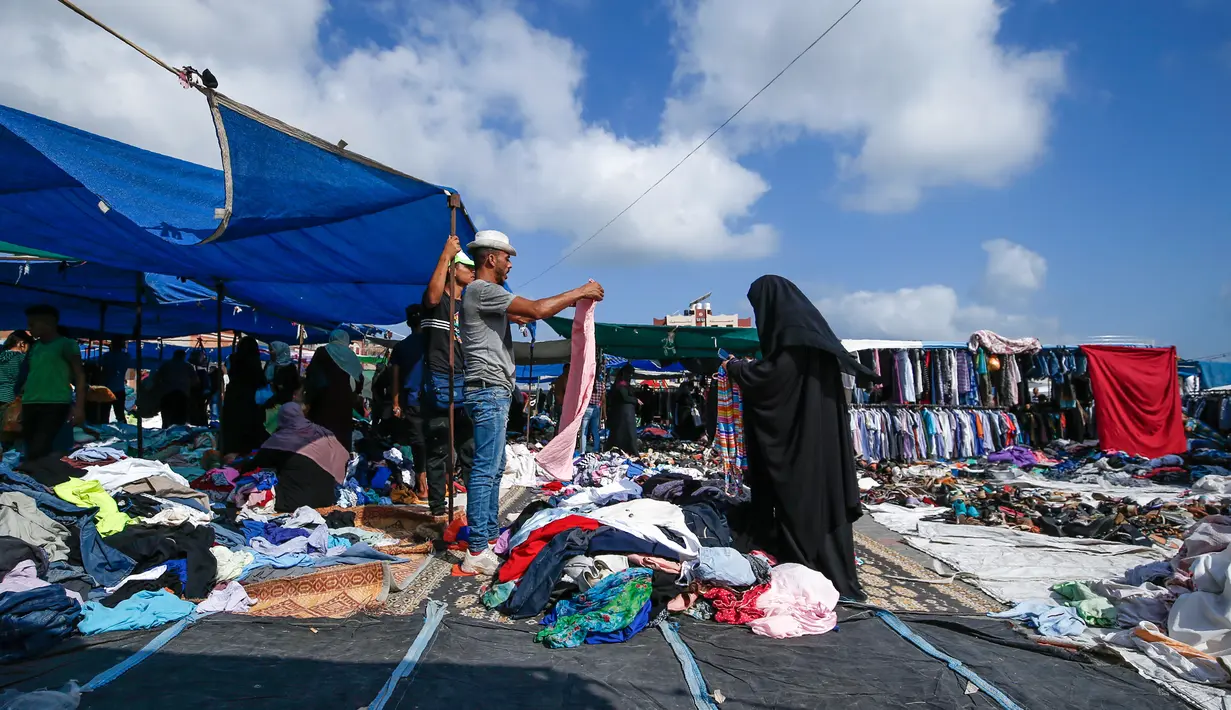 Seorang wanita Palestina berbelanja pakaian di sebuah pasar tradisional yang kembali dibuka setelah pelonggaran karantina wilayah di kamp pengungsi Nuseirat di Jalur Gaza tengah, Senin (13/7/2020). (AFP/Mohammed Abed)