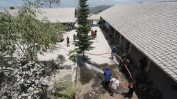 Petugas pemadam kebakaran membersihkan sekolah dari abu setelah Gunung Merapi meletus di Boyolali, Jawa Tengah pada 13 Maret 2023. Pembersihan abu untuk menghindarkan para siswa serta guru dari gangguan abu vulkanik yang ada di kompleks sekolah. (AFP/Dika)