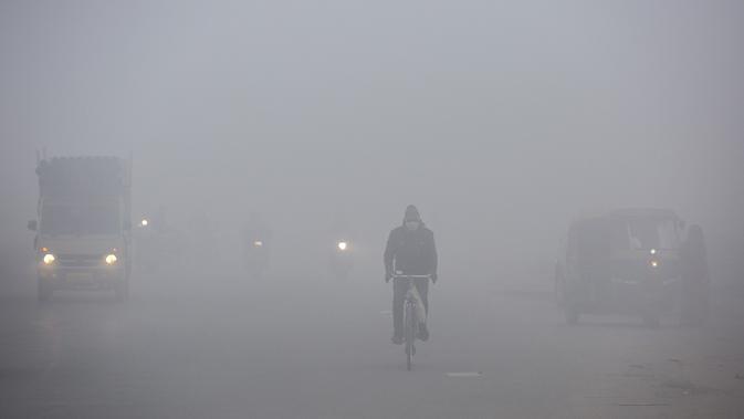 Seorang pria bersepeda di jalan yang diselimuti kabut tebal pada pagi yang dingin di pinggiran New Delhi, India (1/1/2021). Observatorium Safdarjung Delhi, yang menyediakan data perwakilan kota, mencatat suhu minimum 1,1 derajat Celcius, terendah dalam 15 tahun. (AP Photo/Altaf Qadri)