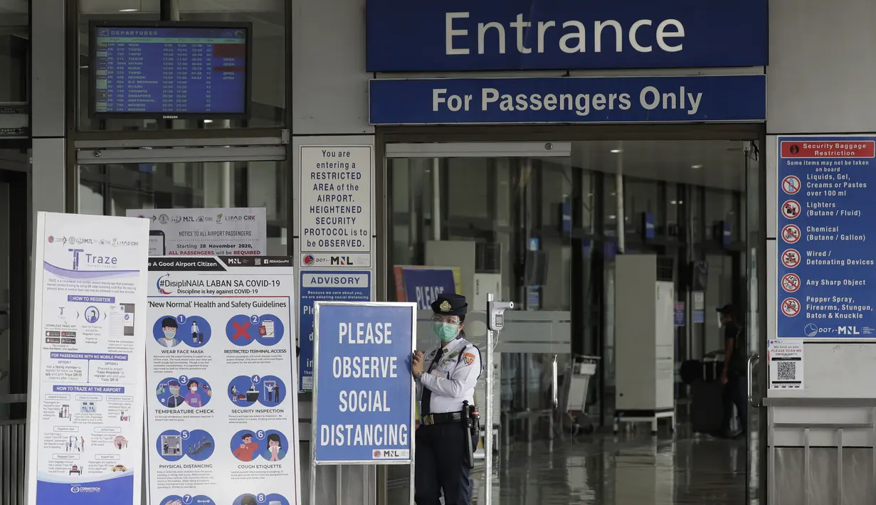 Petugas keamanan berdiri di samping pengingat protokol kesehatan COVID-19 yang ditempatkan di pintu masuk Bandara Internasional Manila, Rabu (17/3/2021). Kedatangan penumpang di bandara internasional Manila telah dibatasi maksimal 1.500 per hari antara 18 Maret hingga 19 April. (AP Photo/Aaron Favil
