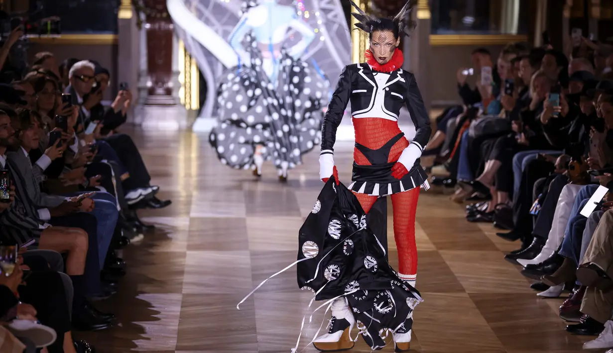 Bella Hadid mempersembahkan kreasi Thom Browne saat peragaan busana Musim Semi-Musim Panas 2023 sebagai bagian dari Paris Womenswear Fashion Week, Paris, Prancis, 3 Oktober 2022. Bella menambahkan sepasang sarung tangan merah dan meninggikan tinggi badannya dengan sepasang sepatu hak tinggi bertali hitam dengan kaus kaki wol berbintik-bintik. (Photo by Vianney Le Caer/Invision/AP)