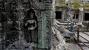 Wisatawan berpose saat mengunjungi kompleks kuil Ta Prohm di provinsi Siem Reap, Kamboja. Kombinasi menarik dan atmosfer pohon yang tumbuh keluar dari reruntuhan kuil serta hutan yang mengelilinginya menjadikan kuil ini populer di Kamboja. (REUTERS/Samrang Pring)