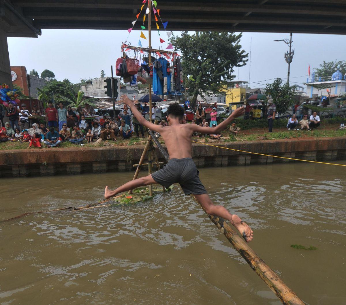 Seorang peserta mencoba melewati bambu yang telah dilumuri oli untuk mencapai pinang dalam lomba Titian Bambu di aliran Kalimalang, Jakarta Timur, Sabtu (24/8/2024). Semangat perayaan HUT ke-79 Kemerdekaan RI masih terasa di lingkungan RW 04 Kelurahan Cip