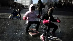 Sejumlah anak bermain di sungai yang membeku di Beijing, China (21/1). Akibat membeku, Sungai ini menjadi objek wisata dadakan yang banyak diminati wisatawan. (AFP/Fred Dufour)