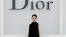 Mitsuki Takahata memilih dress pleated hitam dengan detail bunga yang statement. Dipadukan anting hoop dan tas mini hitam [dok. Dior]