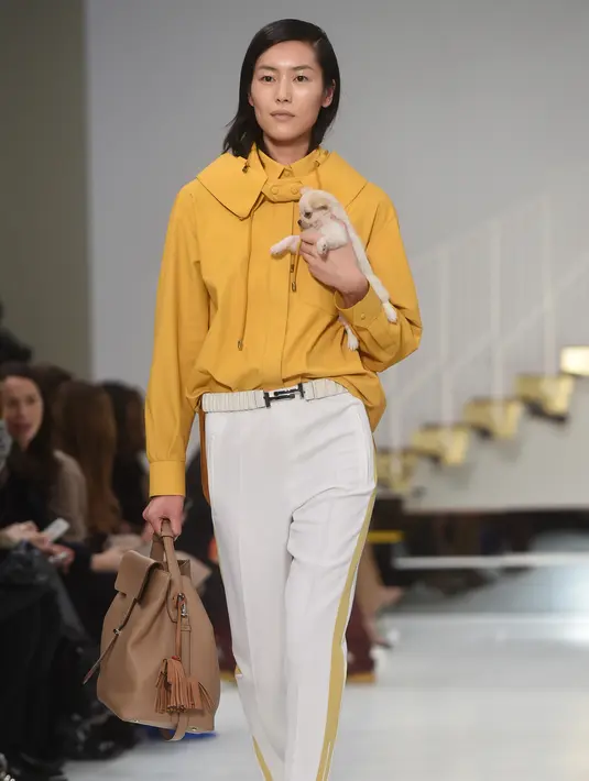 Seorang model menggendong anak anjing saat memamerkan rancangan Tod's di Milan Fashion Week, Milan, Italia, Jumat (23/2). Selain Gigi Hadid, para model Tod's lainnya juga membawa anak anjing saat tampil di Milan Fashion Week. (Filippo MONTEFORTE/AFP)