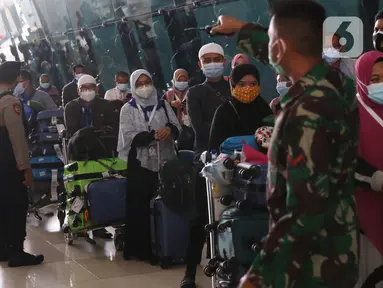Petugas mengarahkan rombongan jemaah umrah yang tiba di Bandara Soekarno Hatta, Tangerang, Selasa (29/12/2020). Rombongan jemaah umrah yang baru tiba di Indonesia tersebut diarahkan untuk melakukan karantina di tempat yang telah disediakan oleh pemerintah. (Liputan6.com/Angga Yuniar)