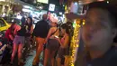 Foto pada 11 Oktober 2018 menunjukkan turis asing  berjalan melewati sekumpulan wanita di Nana Red Light Distrik, Bangkok, Thailand. Nana Red Light District memang dikenal sebagai kawasan hiburan malam terbesar di Bangkok. (Romeo GACAD / AFP)
