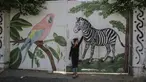 Seorang gadis Palestina menyentuh mural zebra di luar kebun binatang lokal yang ditutup di Rafah di Jalur Gaza selatan (26/5/2020). Kebun binatang itu ditutup selama liburan Idul Fitri karena pandemi virus coronavirus COVID-19. (AFP/Said Khatib)