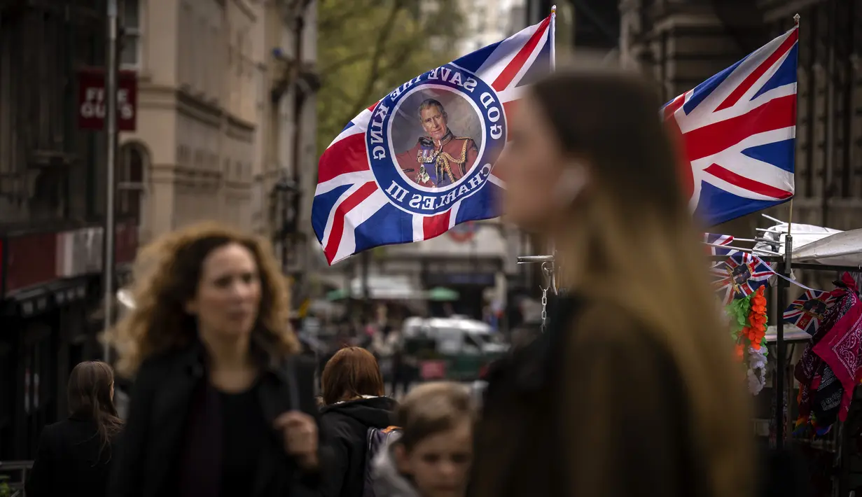 Pejalan kaki berjalan melewati kios yang menjual bendera yang mengumumkan penobatan Raja Charles di London, Jumat, 5 Mei 2023. Penobatan Raja Charles III akan berlangsung di Westminster Abbey pada 6 Mei. (AP Photo/Emilio Morenatti)