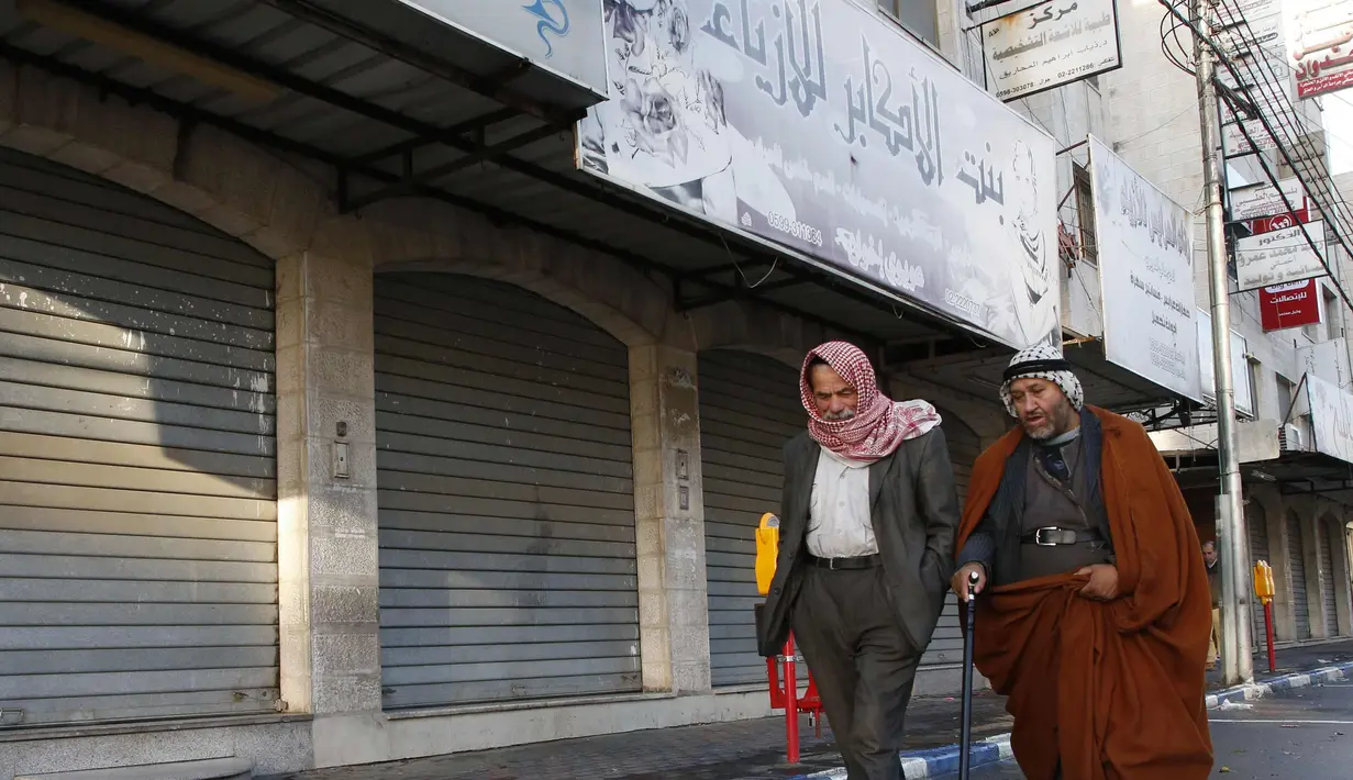 Warga Palestina berjalan melewati toko-toko yang tutup di kota Nablus, Tepi Barat, (7/12). Usai Presiden AS, Donald Trump mengumumkan Yerusalem sebagai ibu kota Israel suasana sepi terlihat di kawasan tersebut. (AFP Photo/Hazem Bader)