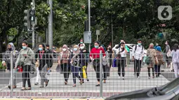 Orang-orang menyeberang jalan di kawasan Sudirman, Jakarta, Rabu (16/12/2020). Pemprov DKI bakal memberlakukan kebijakan WFH (work from home) bagi ASN sebesar 75 persen untuk mengantisipasi lonjakan kasus konfirmasi positif Covid-19 pada akhir tahun. (Liputan6.com/Faizal Fanani)