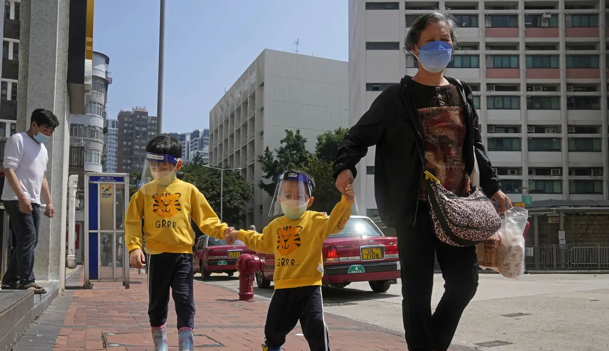 Seorang wanita dan anak-anak yang mengenakan masker dan pelindung wajah berjalan di jalan di Hong Kong, Jumat (4/3/2022). Pemimpin Hong Kong awal pekan ini mengatakan mobilitas orang mungkin dibatasi selama tes covid-19 massal wajib ketika kasus harian mencapai rekor. (AP Photo/Kin Cheung)