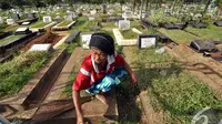 Seorang pengurus makam membersihkan salah satu kuburan yang mulai ditumbuhi rumput liar di TPU Karet Bivak, Jakarta, Minggu (11/1/2015). (Liputan6.com/Miftahul Hayat)
