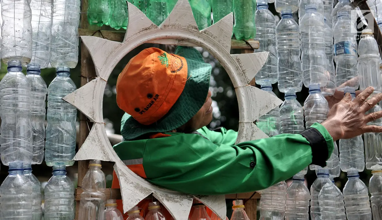 Petugas UPK Badan Air DLH DKI Jakarta saat merapikan instalasi botol yang menghiasi pos di Pasar Rebo, Jakarta, Selasa (12/3). Lebih dari seribu botol plastik bekas dipasang untuk menghiasi Pos  UPK Badan Air di Pasar Rebo. (merdeka.com/Iqbal Nugroho)