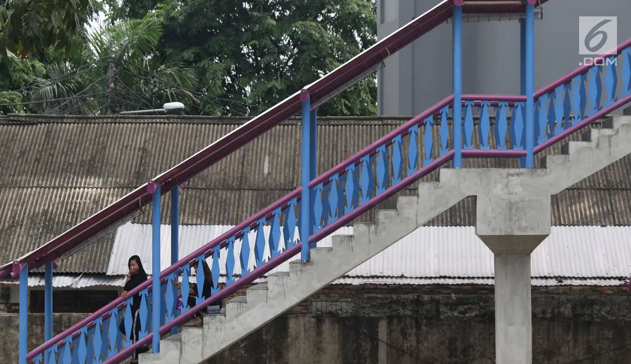Warga berteduh di lajur naik turun JPO Jelambar Barat di Jalan Pangeran Tubagus Angke, Jakarta, Sabtu (22/12). Pagar pembatas JPO Jelambar Barat juga dihias dengan ornamen gigi balang khas budaya Betawi. (Liputan6.com/Helmi Fithriansyah)