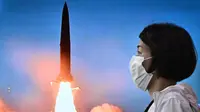 Seorang perempuan berjalan melewati layar yang menunjukkan siaran berita dengan rekaman file uji coba rudal Korea Utara, di stasiun kereta api di Seoul, Minggu (5/6/2022). Peluncuran itu dilakukan sehari setelah angkatan laut Korea Selatan dan Amerika Serikat menyelesaikan latihan gabungan tiga hari di perairan Okinawa Jepang. (Anthony WALLACE / AFP)