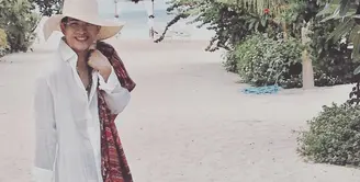 Oscar Lawalata yang sudah mengganti namanya Asha Smara Darra punya gaya simple dan stylish saat liburan di pantai. Seperti tunik kerah kemeja dengan topi lebar, syar warna cerah, serta totebag. (Foto: Instagram/oscarlawalata)