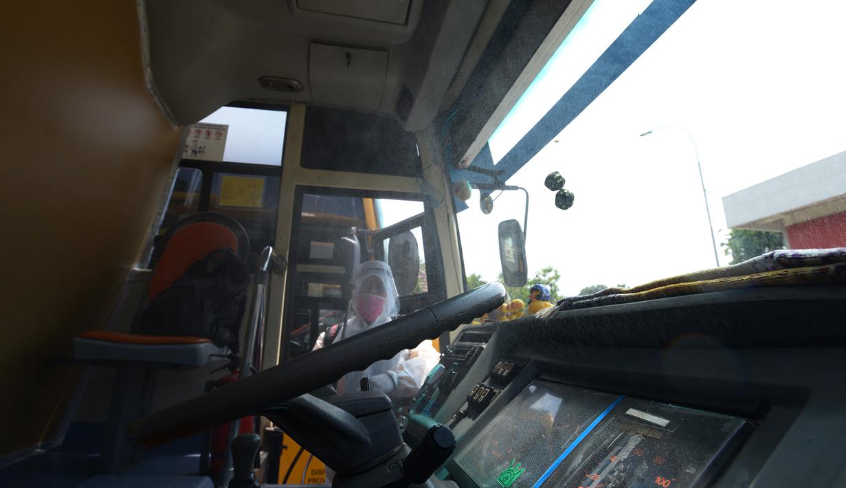 Petugas ber-APD menyemprotkan disinfektan pada bus sekolah di Posko Gabungan PSBB dan Gakplin Protkes, Puskesmas Jatinegara, Jakarta, (22/9/2020). Sejumlah unit bus sekolah kini dialihfungsikan menjadi kendaraan untuk mengantar pasien Covid-19 berstatus OTG menuju Wisma Atlet. (merdeka.com/Imam Buho