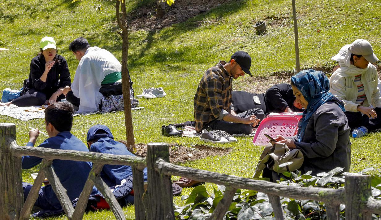 Orang-orang duduk di sebuah taman saat warga Iran berpiknik di luar rumah bersama keluarga dan teman untuk menandai "Sizdeh Bedar" (Hari Alam), 13 hari setelah tahun baru Nowruz Persia, di utara Teheran, Minggu (2/4/2023). (Photo by AFP)