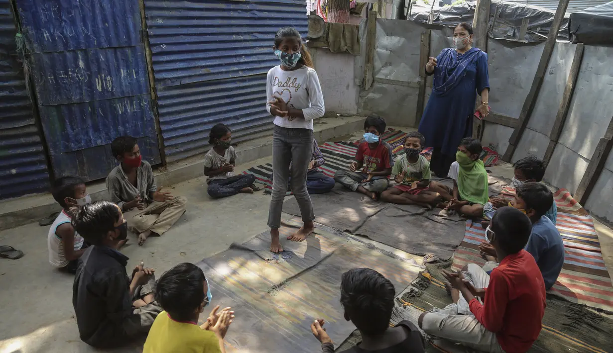 Seorang guru memberi isyarat saat anak-anak mengenakan masker sebagai tindakan pencegahan terhadap virus corona menghadiri kelas online di sebuah perkampungan kumuh di pinggiran Jammu, India, Senin, 14 Juni 2021. (AP Photo/Channi Anand)