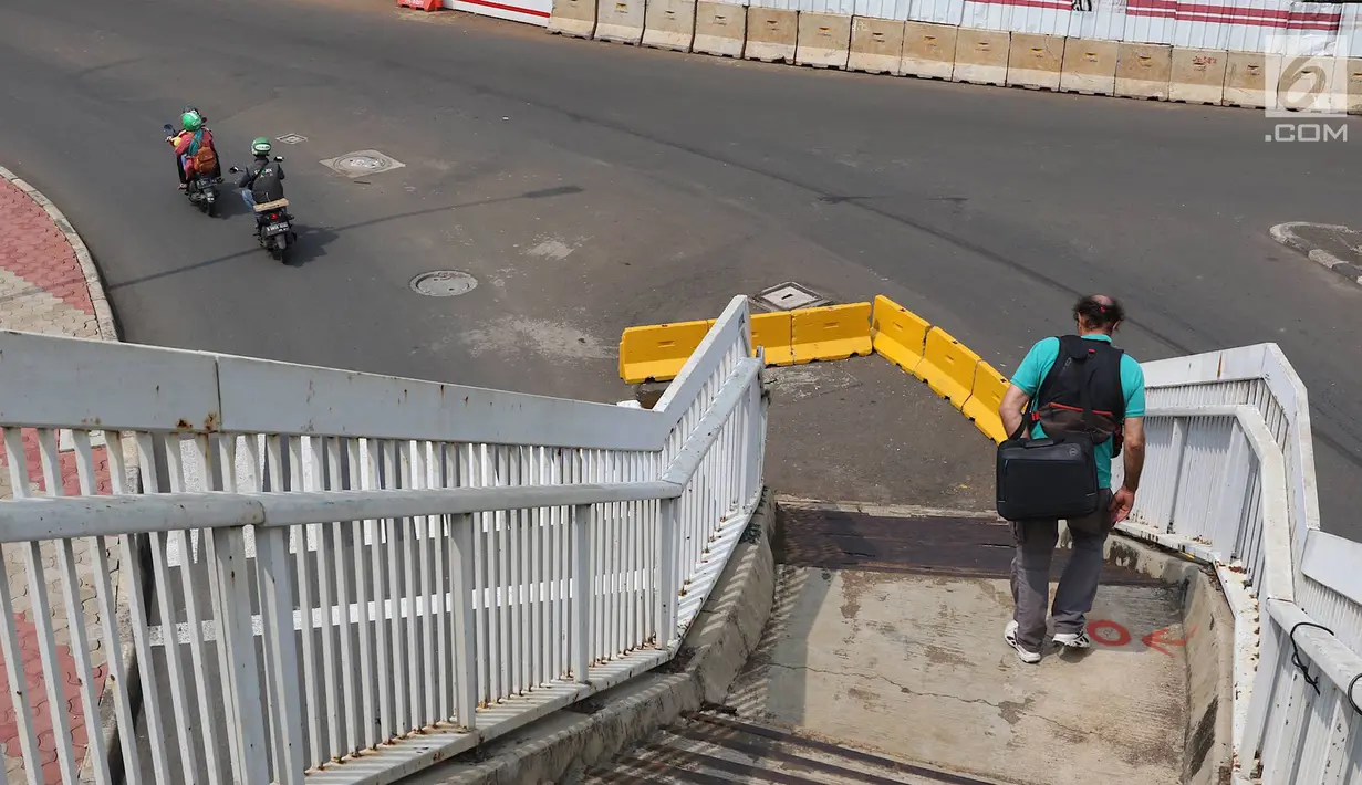 Pejalan kaki menuruni tangga JPO yang berada di tengah jalan Dewi Sartika, Jakarta, Rabu (9/1). Adanya proyek pelebaran jalan menyebabkan posisi trotoar bergeser sehingga tangga JPO menjadi di tengah jalan. (Liputan6.com/Immanuel Antonius)