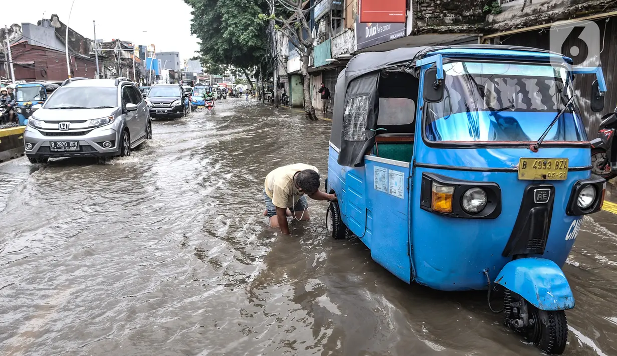 Seorang pria memeriksa ban bajaj saat banjir menggenangi Jalan Jatinegara Barat, Jakarta, Senin (8/2/2021). Selain menyebabkan pertokoan di kawasan itu terpaksa tutup, banjur juga menggangu aktivitas warga. (merdeka.com/Iqbal S. Nugroho)