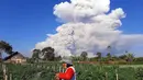 Seorang petani menyemprotkan cairan pestisida pada tanaman saat unung Sinabung memuntahkan abu ke langit, seperti terlihat dari Karo, Sumatera Utara, Selasa (2/3/2021).  Gunung Sinabung, Sumatera Utara, memuntahkan awan panas pada pukul 07.11 WIB, Selasa (2/1/2021). (AFP/Bahari Tarigan)