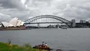 Dua pelari beristirahat di Kursi Nyonya Macquarie yang menghadap ke Opera House dan Harbour Bridge di Sydney, Rabu (30/12/2020). Klaster baru virus korona (Covid-19) muncul di kota Sydney, New South Wales, Australia, menjelang pergantian tahun. (Saeed KHAN / AFP)