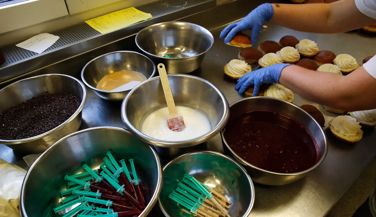 Pekerja menyiapkan berliner (donat Jerman) yang akan dijual dengan jarum suntik penuh raspberry jelly di toko roti Kreyenbuhl di Muri, Swiss, 5 Februari 2021. Merespons hadirnya vaksin Covid-19, toko roti Kreyenbuhl mencoba merayakannya dengan membuat "Vaccine Berliners". (STEFAN WERMUTH/AFP)