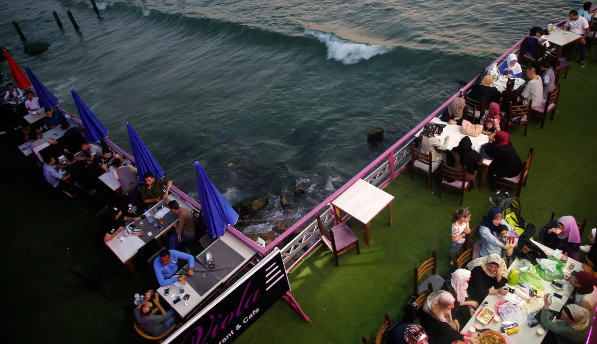 Keluarga Palestina menikmati makanan di sebuah restoran di sepanjang pantai di Kota Gaza (10/6/2019). Pergi ke restoran di dekat pantai merupakan opsi bagi warga Palestina untuk menikmati suasana alam. (AFP Photo/Mohammed Abed)