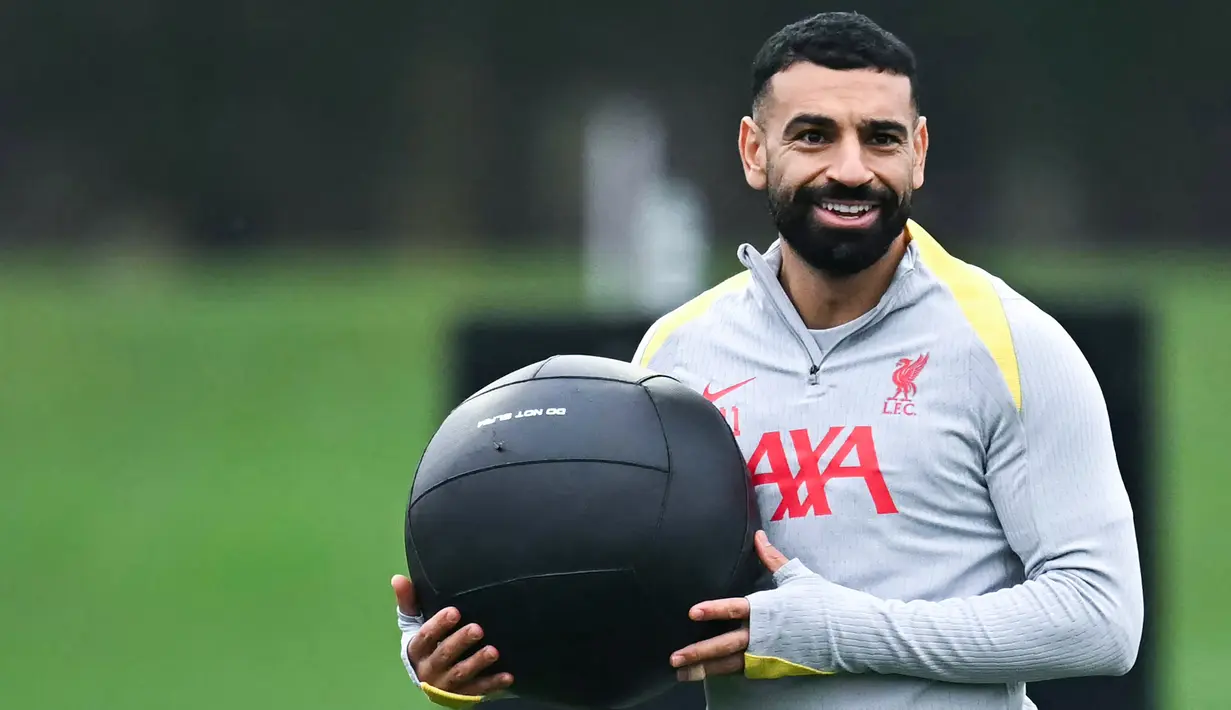 Pemain Liverpool, Mohamed Salah, tersenyum saat melakukan latihan jelang laga melawan Bayer Leverkusen pada pertandingan keempat Liga Champions 2024-2025  di Stadion Anfield. (AFP/Paul Ellis)