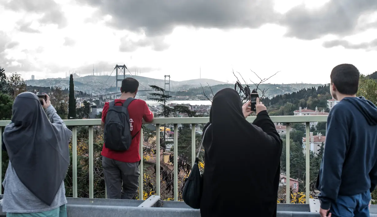 Sebuah keluarga asal Turki mengambil gambar Jembatan Bosphorus di Istanbul pada 11 November 2018. Jembatan Bosphorus menjadi ikon Istanbul bersama bangunan tua bersejarah, seperti Masjid Biru, Aya Sophia, dan sejumlah istana. (BULENT KILIC / AFP)