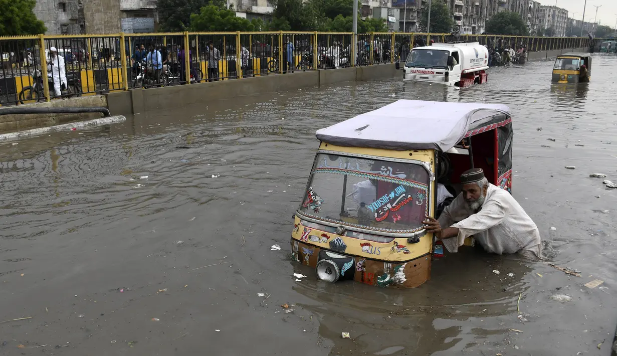 Seorang pengemudi mendorong bajaj saat melewati jalan yang banjir di Karachi, Pakistan, Kamis (23/9/2021). Banjir merendam Karachi setelah diguyur hujan deras. (AP Photo/Fareed Khan)