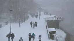 Pejalan kaki berjalan di tepi sungai Thames saat hujan salju melanda London (27/2). Cuaca ekstrem yang melanda sebagian wilayah Eropa menyebabkan warga dan wisatawan mengalami sakit dan beberapa meninggal akibat kedinginan. (AFP Photo/Daniel Leal-Olivas)