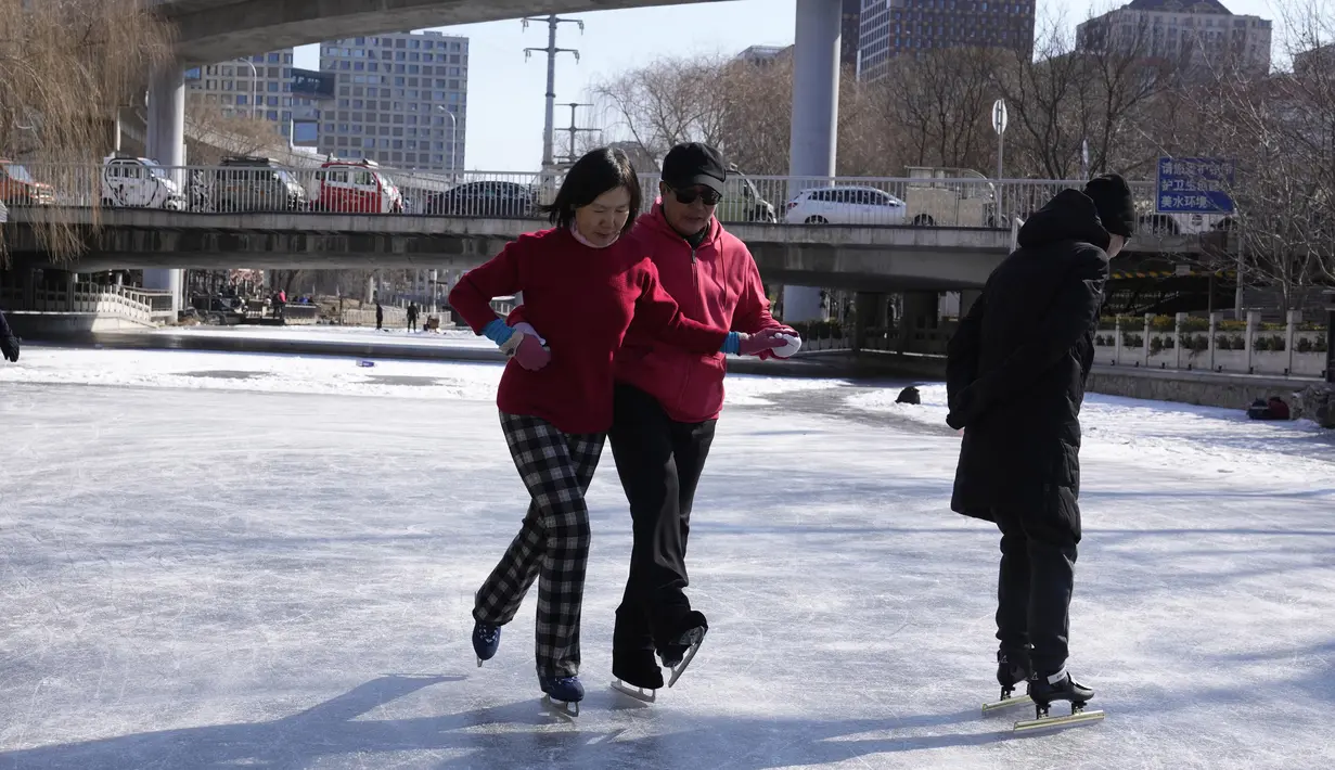 Seorang pria mengajari seorang perempuan menari di atas sepatu roda di kanal yang membeku saat Olimpiade Musim Dingin 2022 hampir berakhir di Beijing pada Sabtu, 19 Februari 2022. (AP Photo/Ng Han Guan)