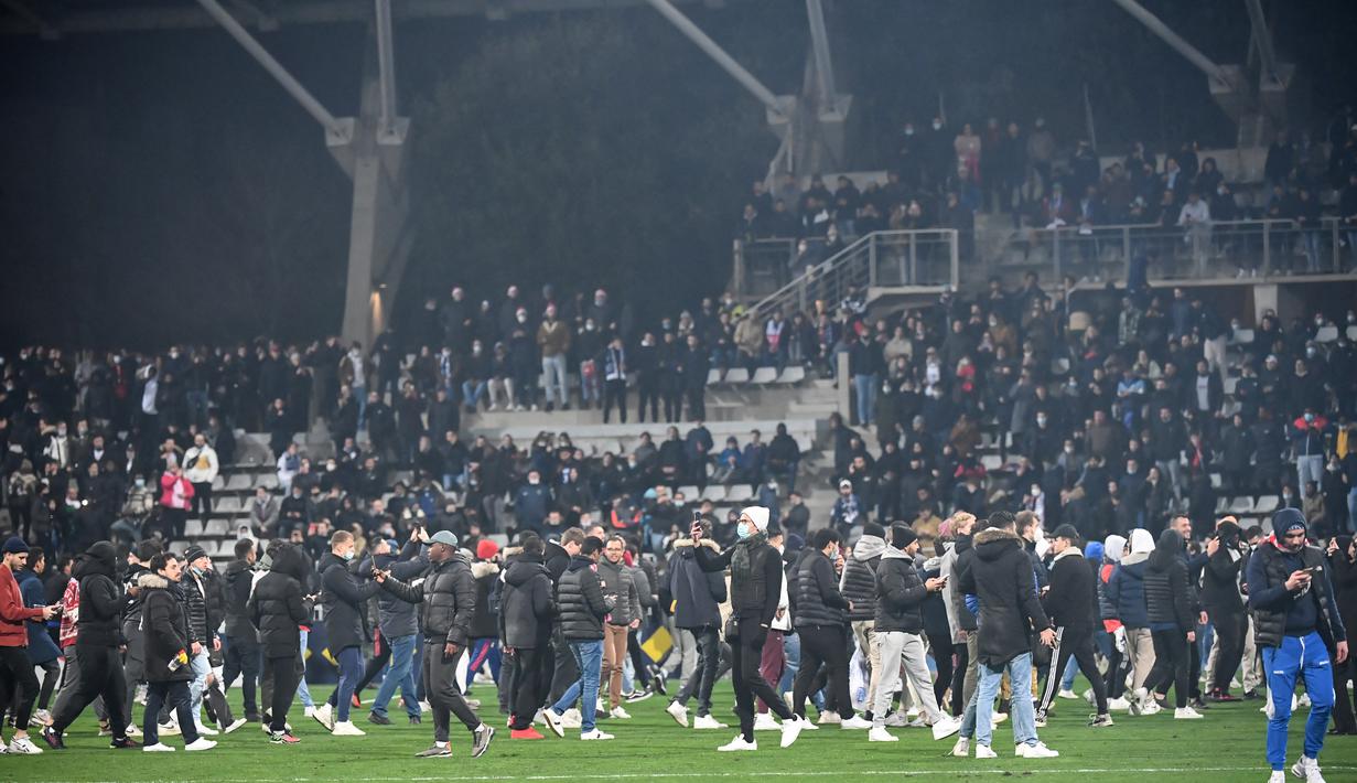Suporter berlarian di lapangan pada babak pertama pertandingan 64 besar Piala Prancis antara Paris FC dan Olympique Lyon di stadion Charlety, Paris, Jumat (17/12/2021). Setelah 45 menit, penyiar stadion datang ke lapangan untuk meminta penggemar meninggalkan arena. (Bertrand GUAY/AFP)